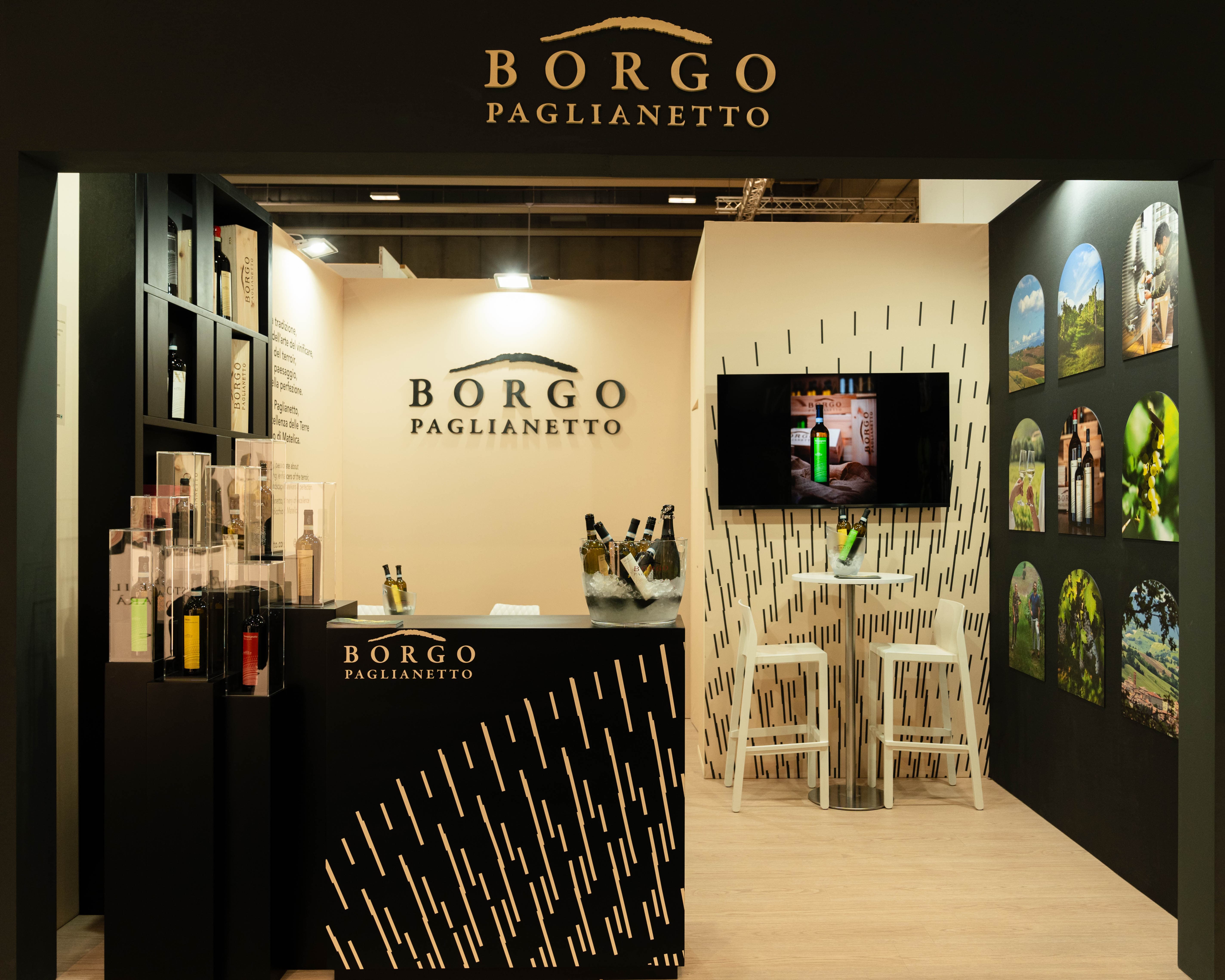 Stand dal design immersivo per Borgo Paglianetto, con pareti grafiche, espositori trasparenti, bottiglie di vino e schermo centrale.